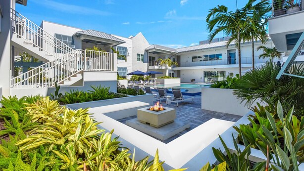 A modern outdoor pool area with lounge chairs, a fire pit, and a staircase leading to a balcony.