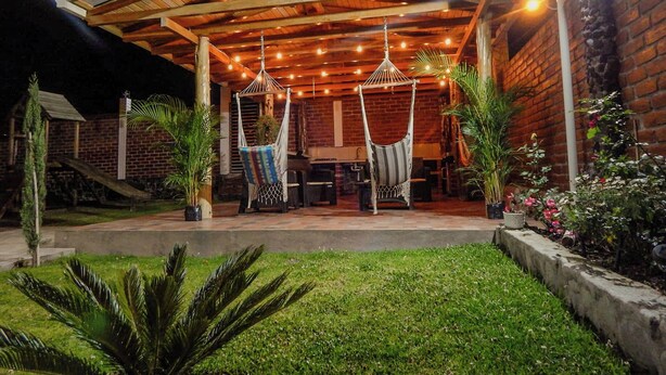 Un patio al aire libre con una pérgola de madera, dos hamacas y plantas en macetas.