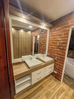 Une salle de bain avec deux lavabos, des meubles en bois, un miroir et un mur en briques.