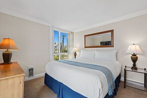 Una habitación de hotel con una cama, dos lámparas de noche, una ventana, un espejo y una mesita de noche de madera.