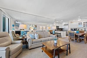 A spacious living room with a sofa, armchair, and coffee table, a dining area with a wooden table and chairs, a kitchen with modern appliances, and a fireplace.