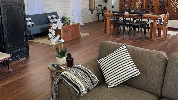 A spacious living room with a wooden floor, a sofa, a dining table with chairs, and a large mirror.