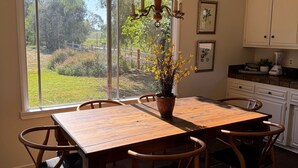 A dining area with a wooden table and chairs, a hanging light fixture, and a view of a garden through large windows.