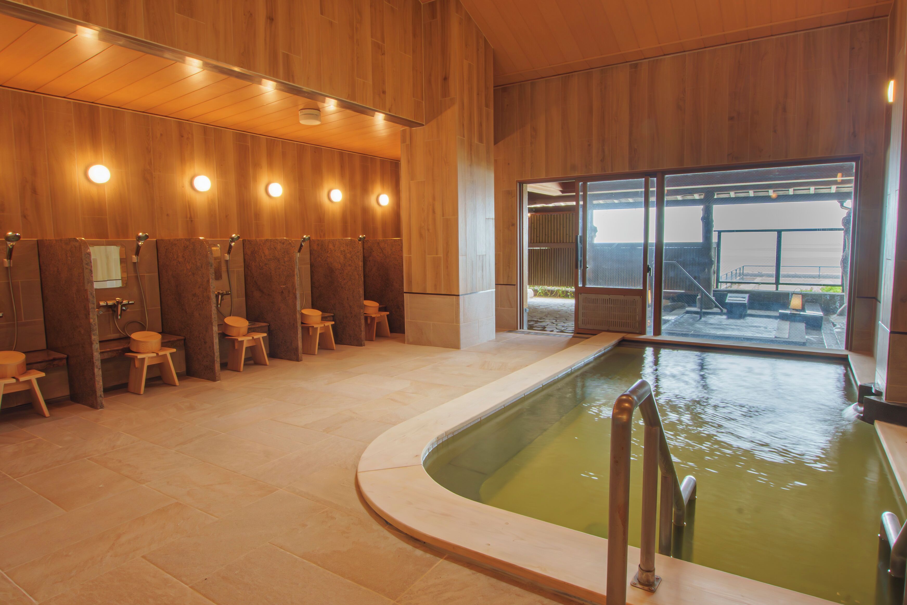 A modern spa area with wooden walls, a pool, and multiple shower stalls.