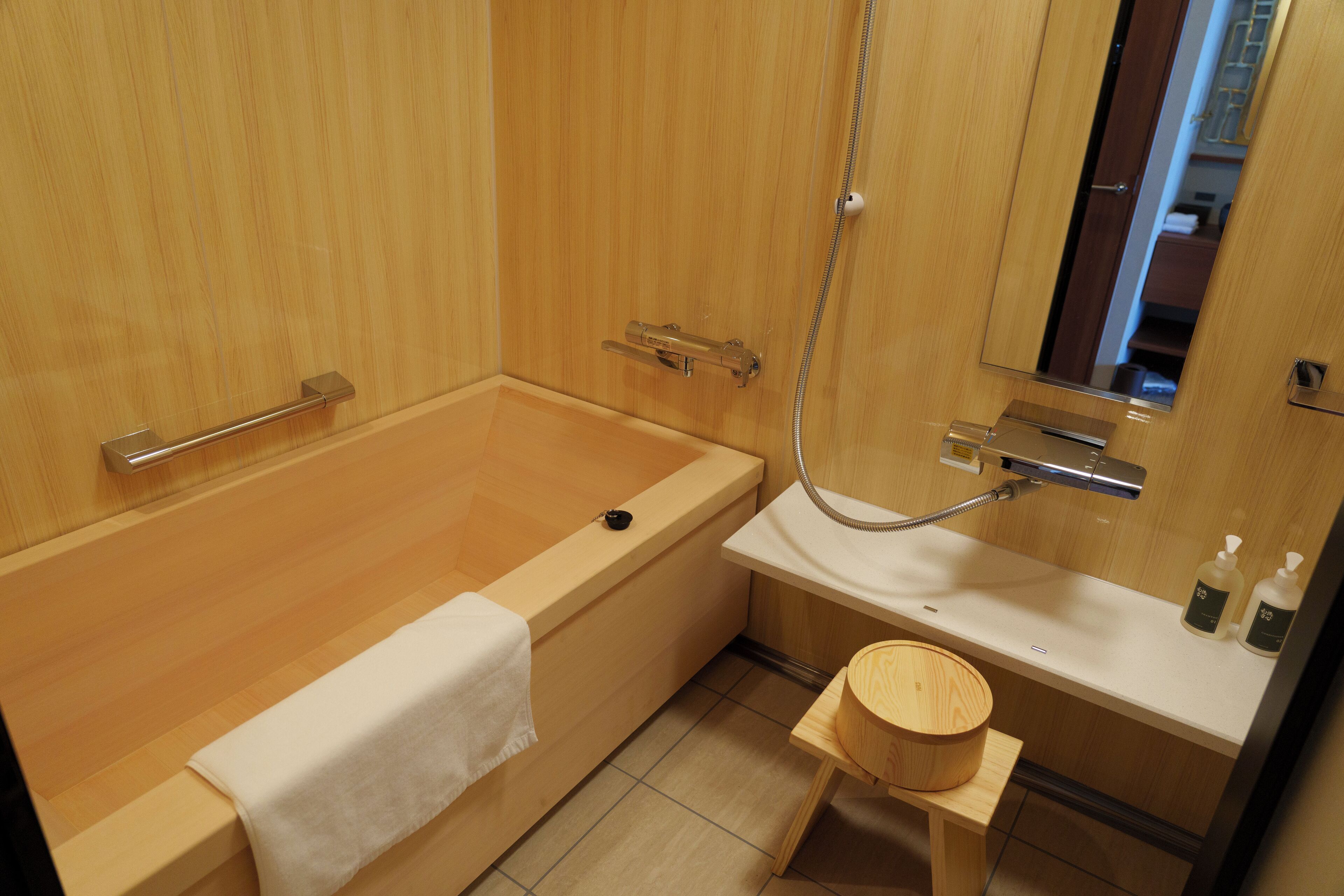A wooden bathroom with a bathtub, a small wooden stool, and a mirror.
