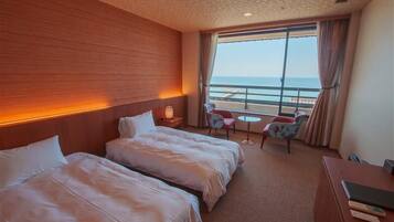 Une chambre d’hôtel avec deux lits, une petite table avec des chaises, un bureau avec une chaise et une grande fenêtre donnant sur la mer.