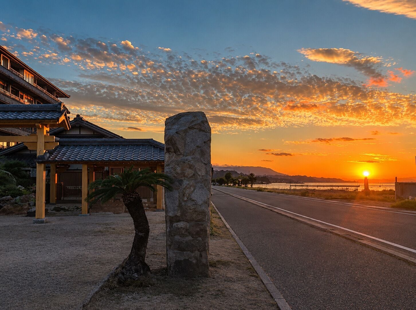 Un edificio tradicional con un pilar de piedra, una calle empedrada y un atardecer al fondo.