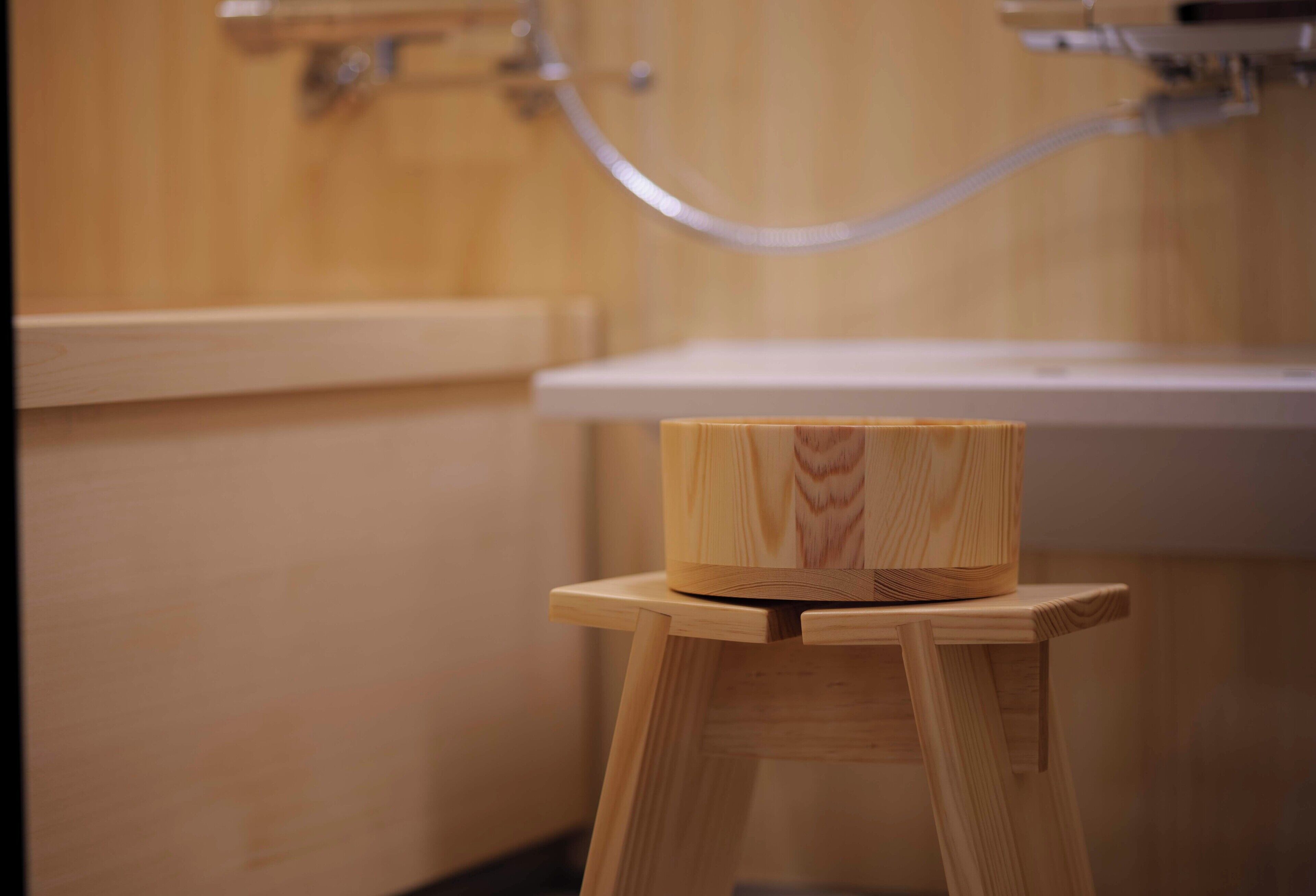 Un tabouret en bois surmonté d’une boîte en bois, dans une salle de bain avec des meubles en bois et un lavabo blanc.