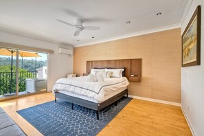 Un dormitorio con una cama grande, un ventilador de techo y vistas a zonas verdes desde el balcón.