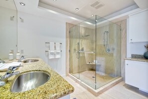 Un baño moderno con ducha de vidrio, encimeras de granito y tocador blanco.