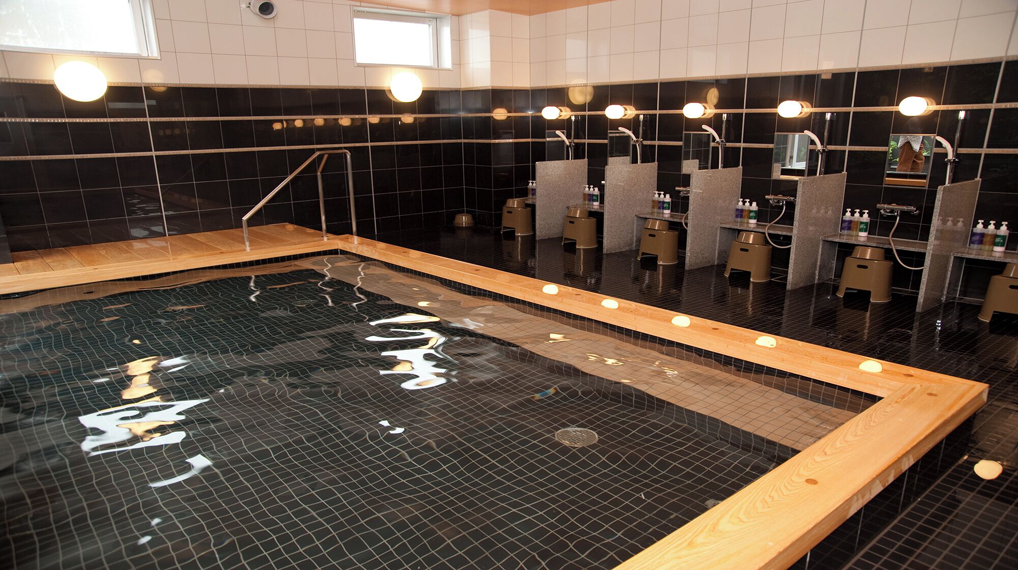 A modern spa with a large hot tub, multiple shower stations, and a tiled floor.