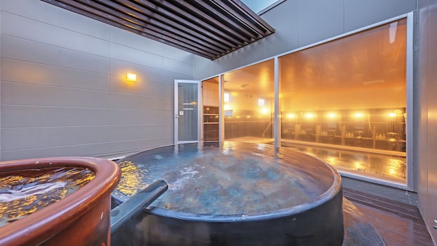 Un área de spa moderna con un jacuzzi, una fuente de agua grande y una sala de sauna con paredes de vidrio.