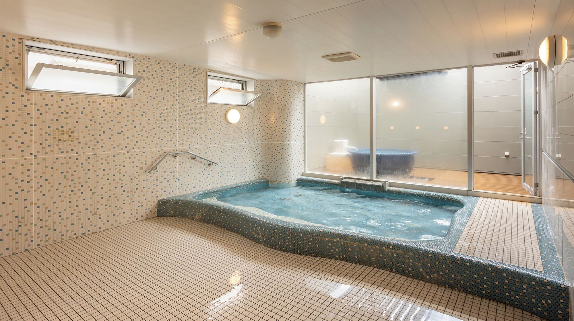 A modern indoor pool area with a hot tub, tiled walls, and a glass door leading to a shower area.