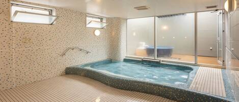 A modern indoor pool area with a hot tub, tiled walls, and a glass door leading to a shower area.