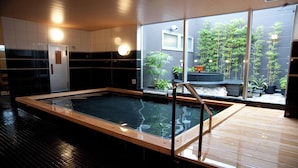 Piscina interior moderna con terraza de madera y vistas a un jardín de bambú a través de amplios ventanales.