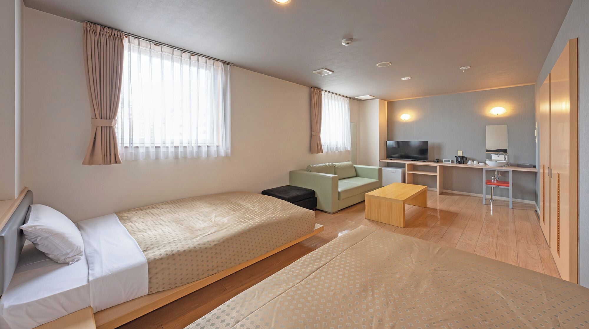 Una habitación de hotel moderna con una cama, un sofá, una mesita, un televisor y un escritorio con un espejo y lavamanos.