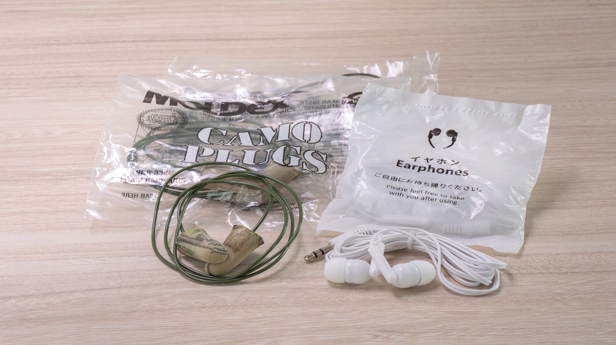 A package of earphones, a pair of earphones, and a charging cable on a wooden surface.