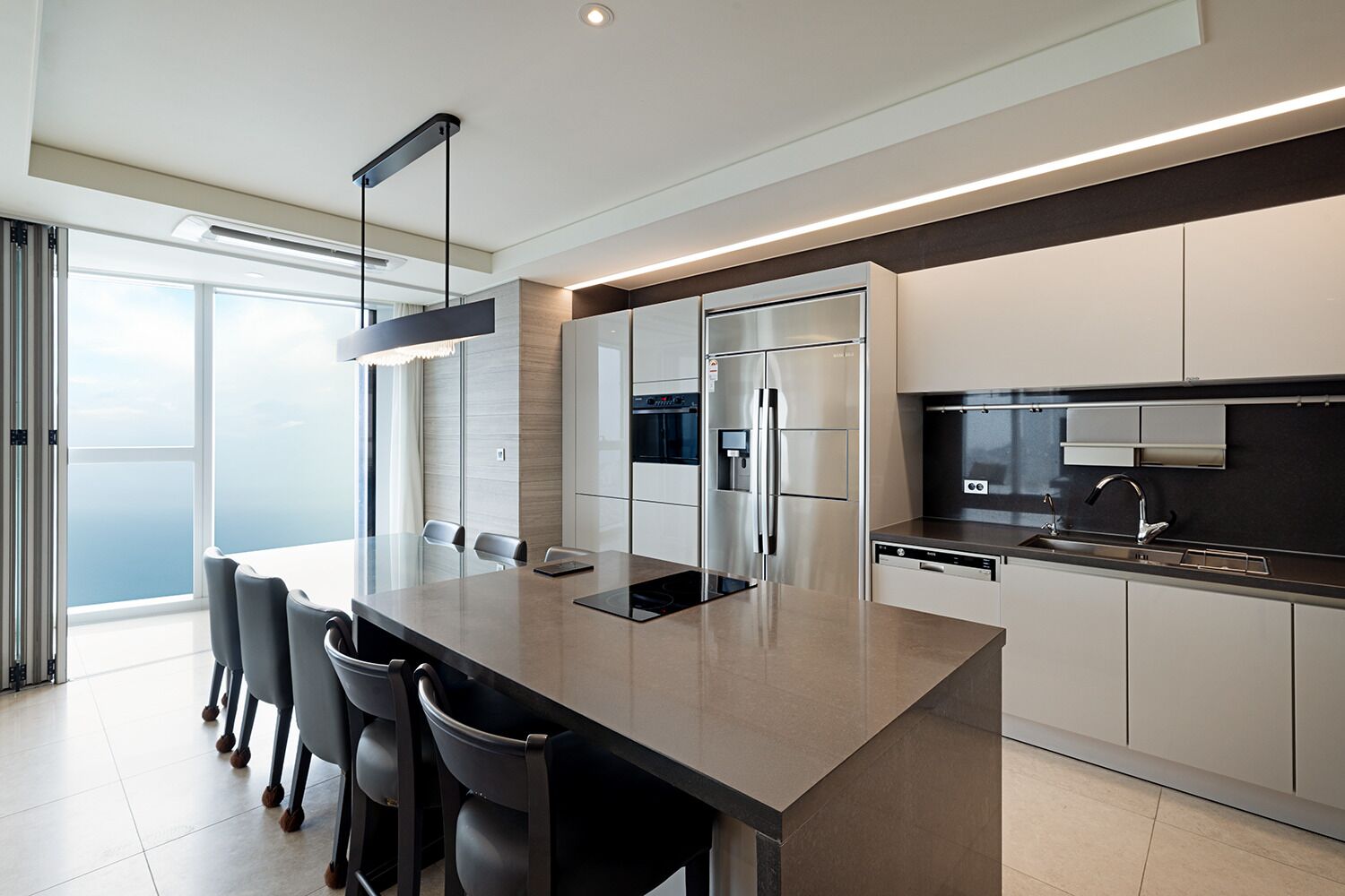 A modern kitchen with a large island, stainless steel appliances, and a view to the outside.