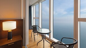 A modern hotel room with a large window offering a view of the sea. There is a round glass table with two chairs and a lamp on a wooden side table. - LCT residence THE VINE Haeundae (Busan)