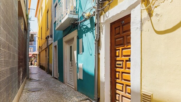 Eine enge Kopfsteinpflasterstraße mit Gebäuden an beiden Seiten, einer blauen Tür und einer gelben Wand.
