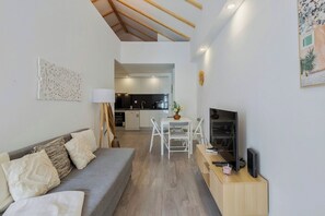 Un salon moderne avec un canapé gris, des chaises blanches, un téléviseur et un meuble en bois.