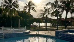 Une piscine dont le bord est revêtu de carrelage, entourée de palmiers et agrémentée d’un kiosque.