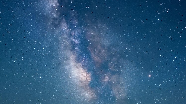 Un ciel nocturne étoilé où l’on peut distinguer une galaxie.