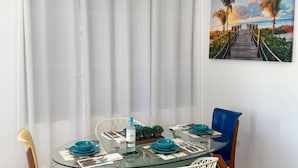 Un coin repas avec une table en verre, des chaises bleues et un rideau blanc.