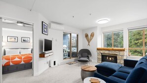 Una sala de estar moderna con un sofá, televisión, chimenea y un ventanal con vistas a árboles.