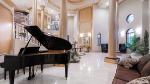 Un piano de cola imponente en un vestíbulo amplio y luminoso, con techos altos y arquitectura clásica, que incluye columnas y una escalera.