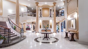 Un lobby espacioso con una imponente escalera, pisos de mármol y columnas de estilo clásico.