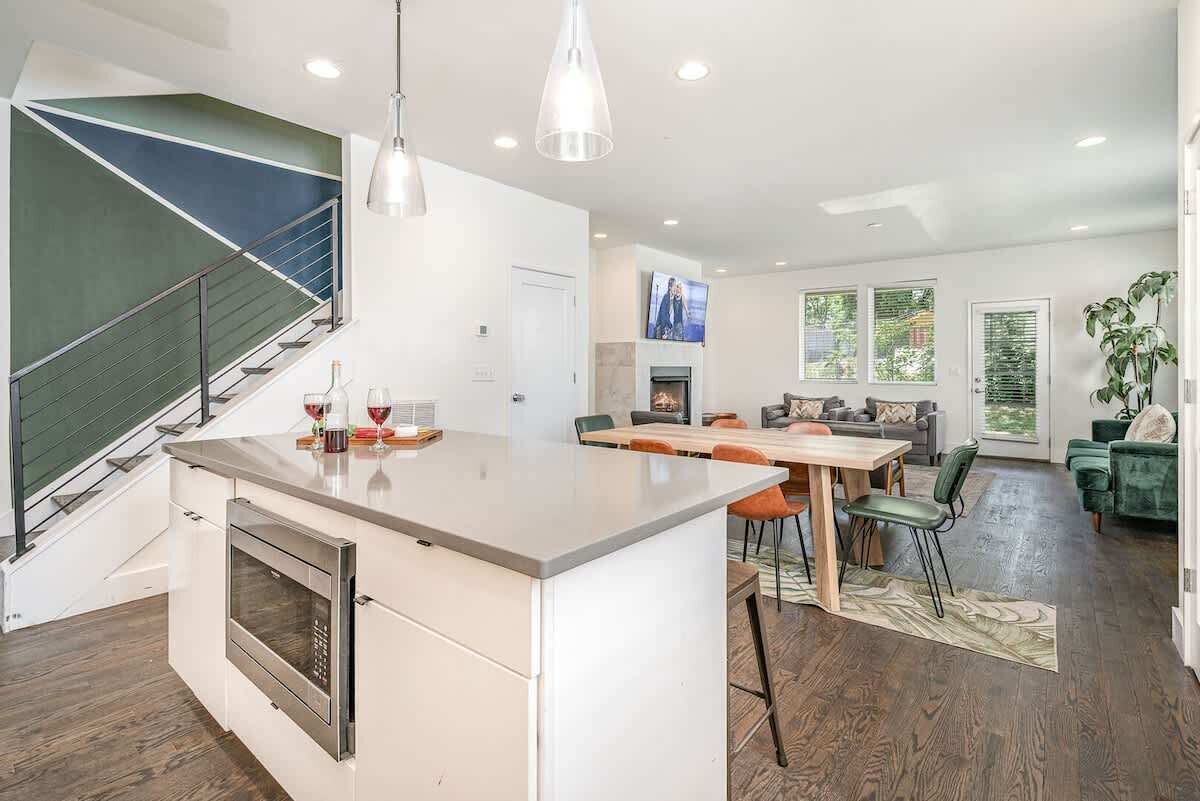 A modern kitchen with a built-in oven, a dining area with a wooden table and chairs, and a staircase with a green accent wall.