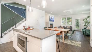 A modern kitchen with a built-in oven, a dining area with a wooden table and chairs, and a staircase with a green accent wall.