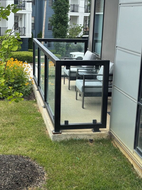 Un espacio exterior moderno con área de estar amurallado con vidrio, piso de concreto y borde con césped.