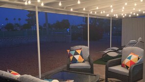 Un espace extérieur aménagé en terrasse, avec des meubles en osier, un tapis à motifs et des guirlandes lumineuses.