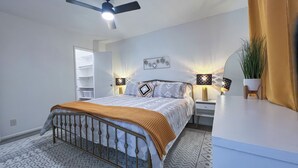 Une chambre à coucher comprenant un lit, des tables de chevet, un ventilateur de plafond, une étagère fixée au mur et une plante en pot.