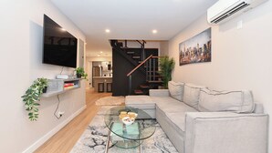 A modern living room with a grey sofa, a glass coffee table, and a flat-screen TV mounted on the wall. - Elegant SoHo 5BR Duplex – Upscale, Central & Spacious (New York)