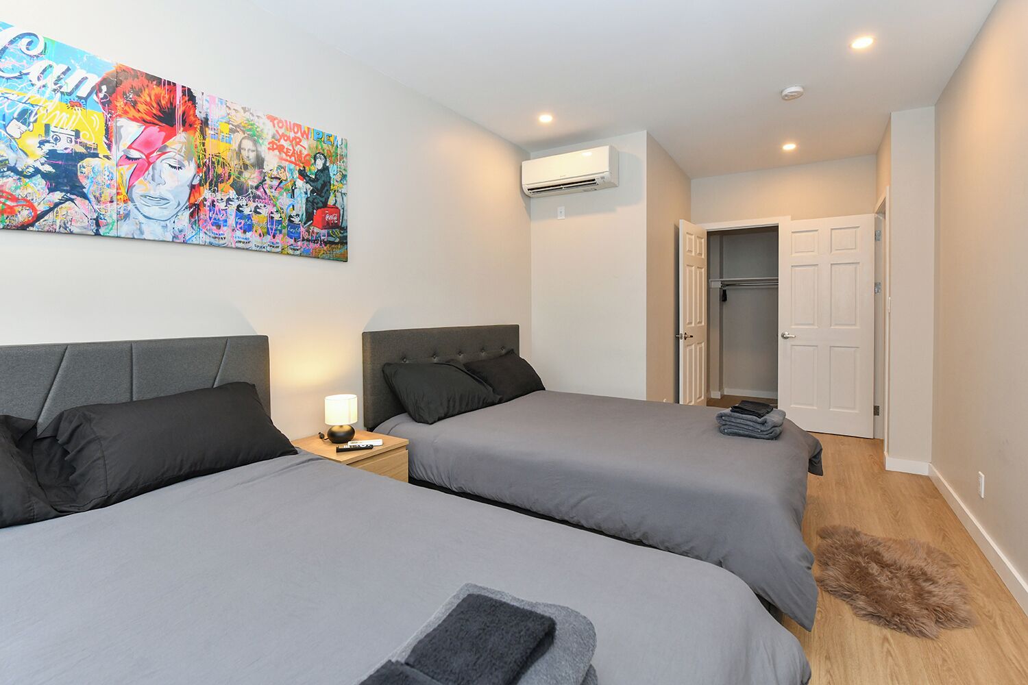 A hotel room with two beds, a large colorful artwork on the wall, an air conditioning unit, and a door leading to a closet.