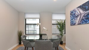 A modern dining area with a glass table, grey chairs, and a potted plant. - Elegant SoHo 5BR Duplex – Upscale, Central & Spacious (New York)