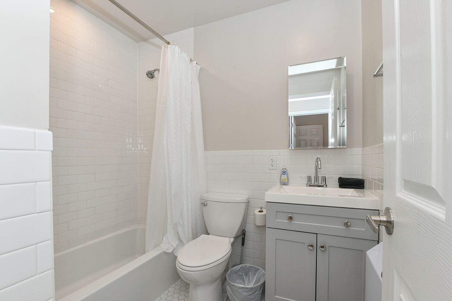 A modern bathroom with white tiles, a shower, a toilet, a sink, and a cabinet.