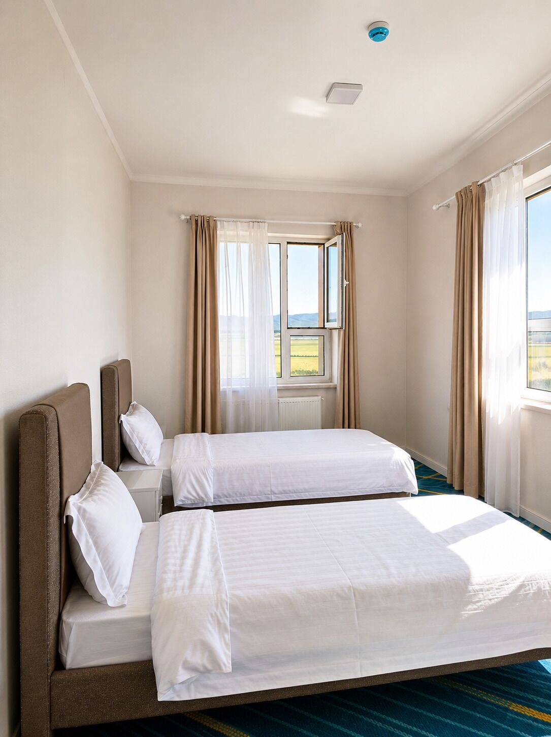A hotel room with two beds, a window with curtains, and a view of the outdoors.