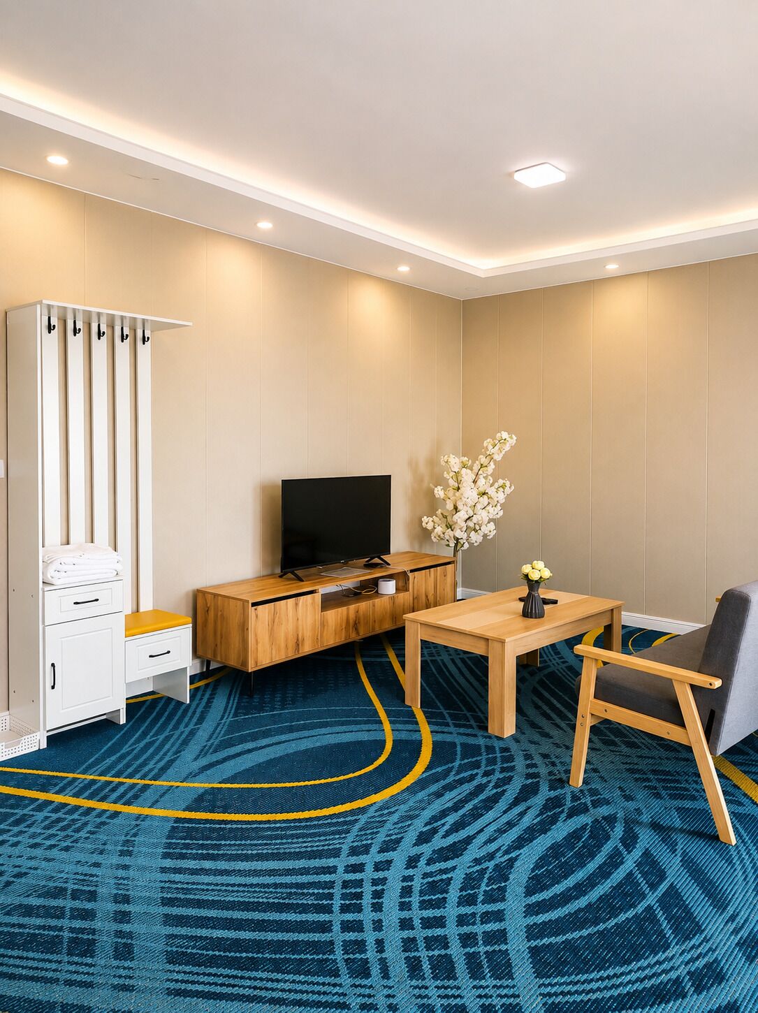 Habitación de hotel con televisión de pantalla plana, escritorio de madera, una silla, armario y alfombra estampada.