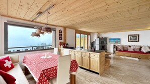A spacious living area with a wooden ceiling, a dining table with a red tablecloth, a sofa with red cushions, and a fireplace. - Mountain Bliss, view and Sauna - Swiss Alps (Anzère)