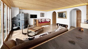 A spacious living room with a fireplace, wooden ceiling, and a large window. - Mountain Bliss, view and Sauna - Swiss Alps (Anzère)