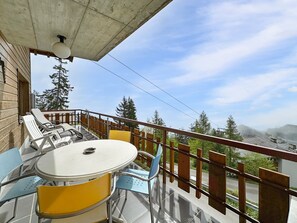 Ein Balkon mit rundem Tisch und Stühlen, der auf eine gebirgige Landschaft blickt.