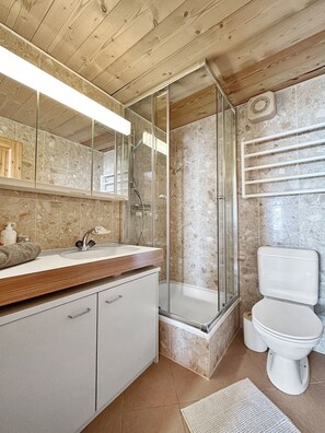 Ein modernes Badezimmer mit Holzboden, einer Duschkabine aus Glas, einer Marmorwand und einem weißen Waschbecken sowie einer Toilette.