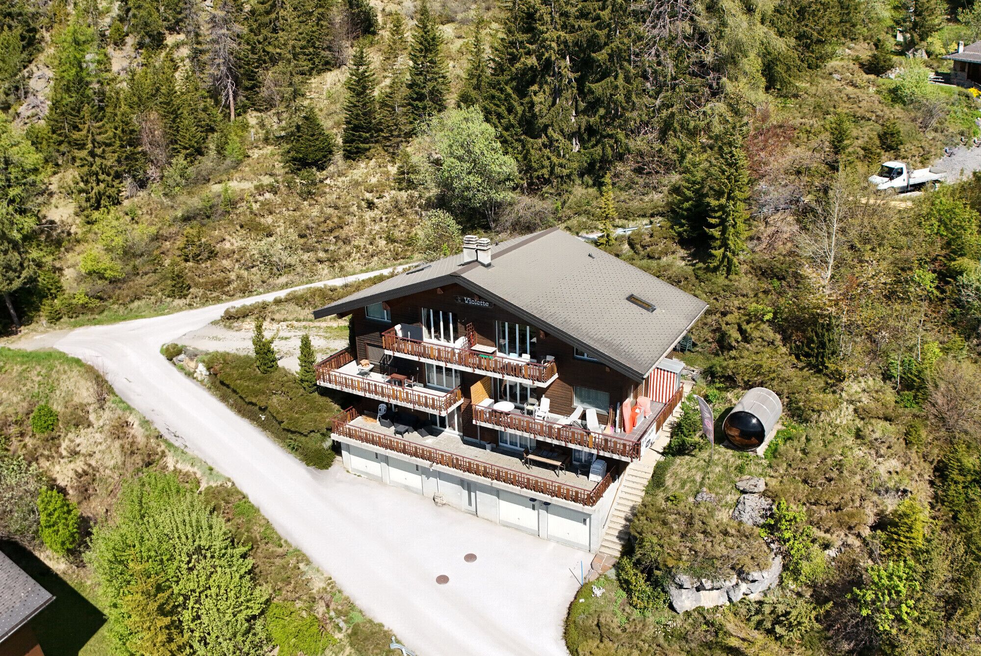 Eine zweistöckige Chalet mit Balkon, an einem Hang gelegen, umgeben von Bäumen.