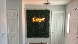 Een gang met een donkere houten vloer, witte deuren en een neonbord op een groene muur met de tekst 'The Waypoint'.
