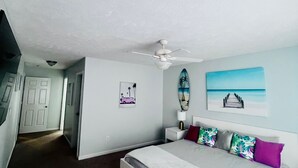 Een slaapkamer met een bed, een plafondventilator, een nachtkastje en een muur met een surfboard en een foto.