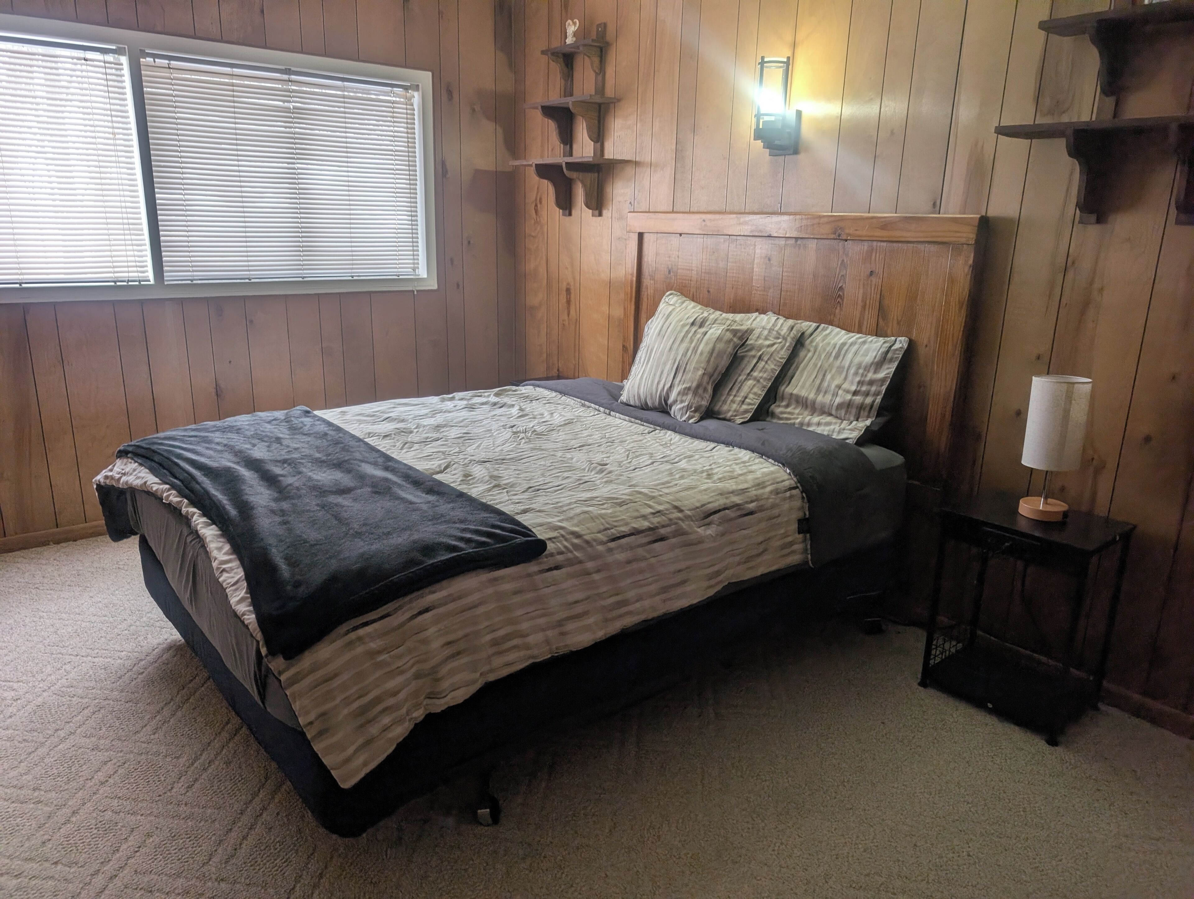 A bedroom with a bed, a nightstand, a lamp, and a window with blinds.
